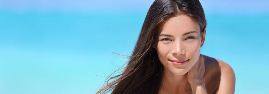 Smiling woman with long hair on a sunny beach with clear blue ocean.